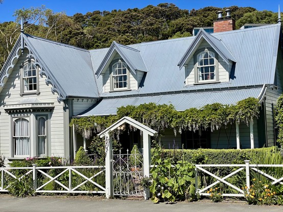 Wooden heritage home with wisteria hanging from the porch & dormer windows projecting from the corrugated iron roof