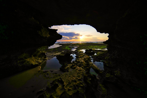 A sunset of beach through a sea cave. Sun at the horizon with pink clouds ⛅️