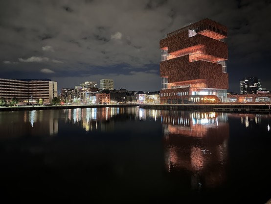 Photo of the MAS museum in Antwerp. Y night, and its reflection in the water in the dock nearby.