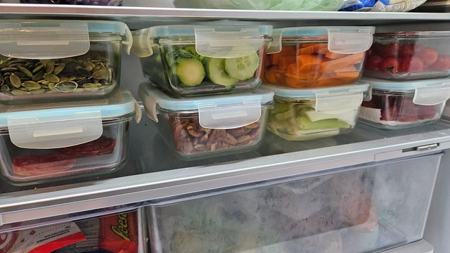 The inside of a fridge showing glass container with cut veggies, fruits and nuts.