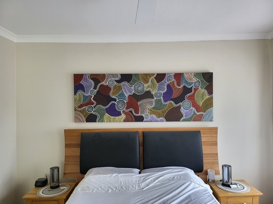 An image of a bed with an Aboriginal painting above it (Gnamma Holes by Shane Hanson)