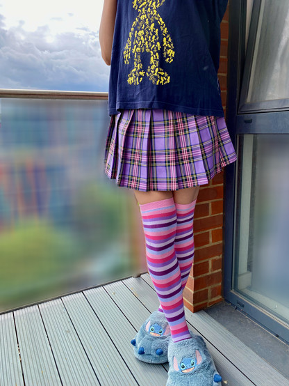 Rina is wearing a purple plaid skirt and purple-and-pink knee-high socks, leaving a sliver of bare thigh visible