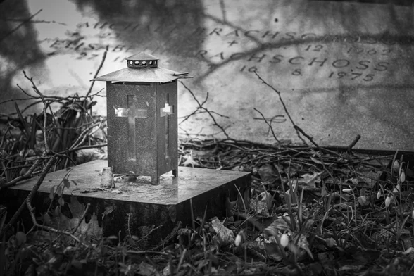a grave light in a lantern with a glass cross in front of a tombstone on an abandoned cemetery. Leavs and dead branches lie on the grave