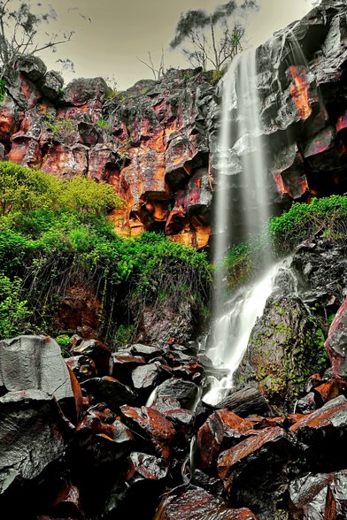A tall waterfall falling along the basalt rock cliff onto a small creek in Victoria Australia