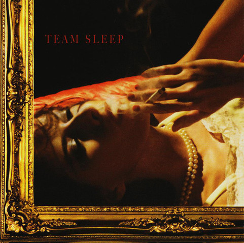 a cover of an album, a woman is laying back on a bed smoking a cigarette, in small red capitol letters it says 'team sleep' she is wearing a pearl necklace, the left and bottom of the image has a fancy gold frame on it