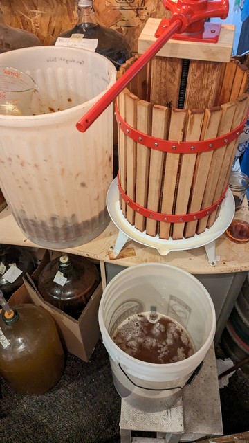 Photo of a fruit press and some buckets, one to collect the juice and one holding the apples waiting to be squeezed