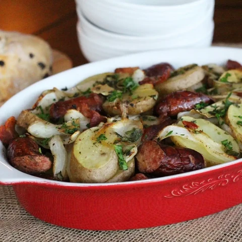 A photo of a broad red serving dish about 5cm deep with a strew of potatoes, bacon, onion and pork sausages inside it