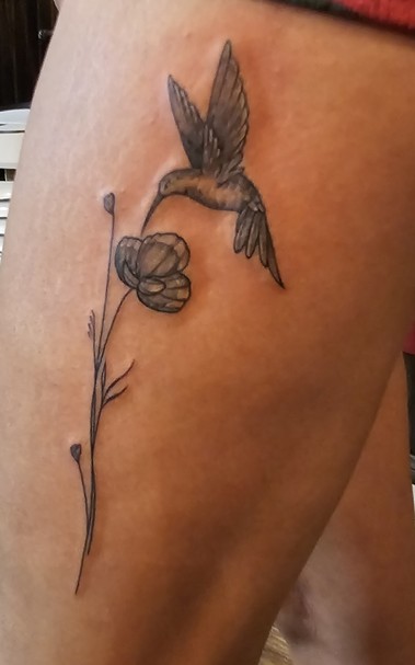 Black and grey tattoo of a hummingbird drinking nectar from a poppy flower