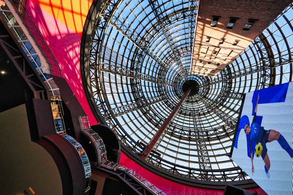 Looking up the dome window of Melbourne central Station. poster of a soccer match on the right. Centre circular dome windows with many rectangles
