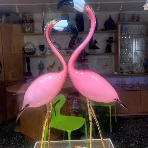 Two large pink glass flamingos stand facing each other with their heads raised. A small green glass cygnet stands at their feet.