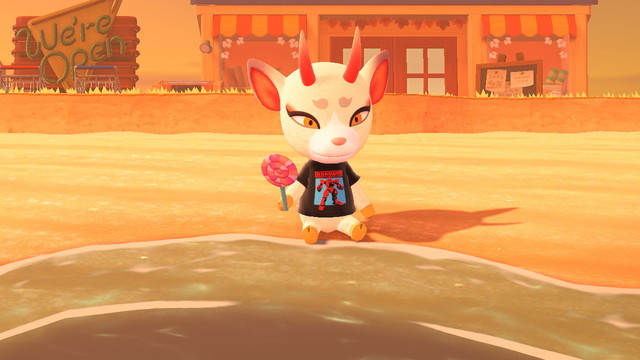 Animal Crossing: New Horizons screenshot. Image of Shino (white deer with long red horns and yellow eyes) sitting on the beach wearing a black t-shirt with a red robot hero on it while holding a cartoonshly large pink swirly lollipop. Behind her is Nook's Cranny and a shut off "We're Open" sign.