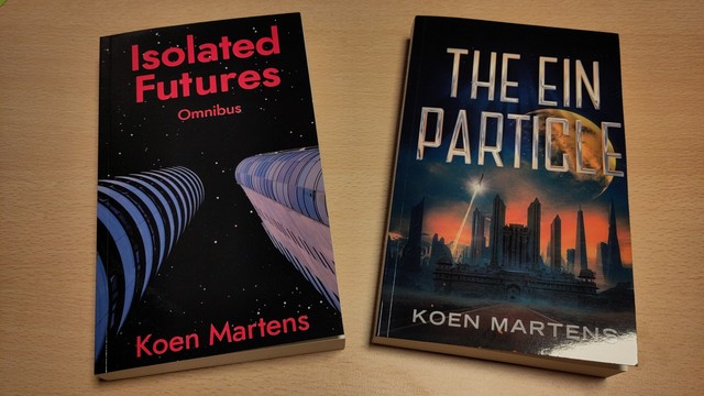 Two books on a desk. On the left we have the Isolated Futures Omnibus, on the right The Ein Particle.
