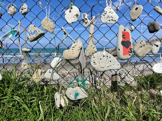 Stones tied to a wire mesh fence, some of which are decorated/ inscribed