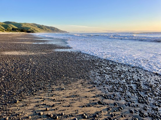 A pebble & sand beach with the glow of early morning sun on the horizon out to sea