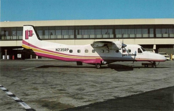 A white prop plane with pink and gold striped and the letter P on the tail is outside of a terminal