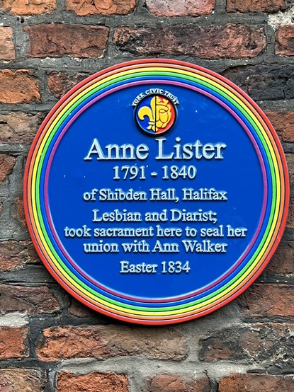 Circular blue plaque with rainbow edging. Text: 
York Civic Trust
Anne Lister
1791-1840
of Shibden Hall, Halifax
Lesbian and diarist,
took sacrament here to seal her
union with Anne Walker
Easter 1834