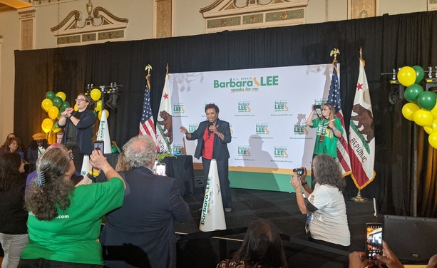 Lee on stage at a rally with green and red balloons