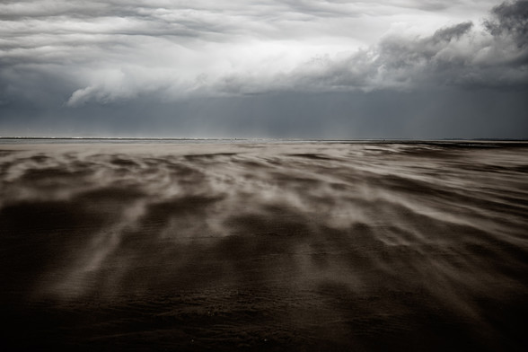 Sand fegt über einen stürmischen Strand vor dunklem Himmel in Ouddorp⁩, NL