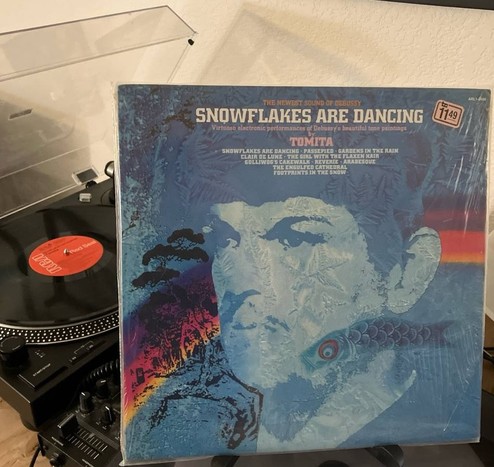 Tomita "Snowflakes Are Dancing" Record sleeve with a portrait of a man in a mustache in mostly blue tones, with a rainbow, stylized trees and a carp streamer. Title and songs are listed at the top.  On the turntable on the background is a record with a red label and RCA visible.