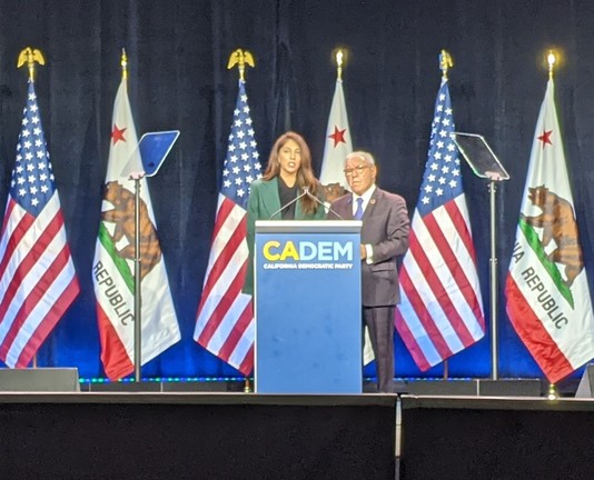 A man and woman standing at a podium in front of California and American flags