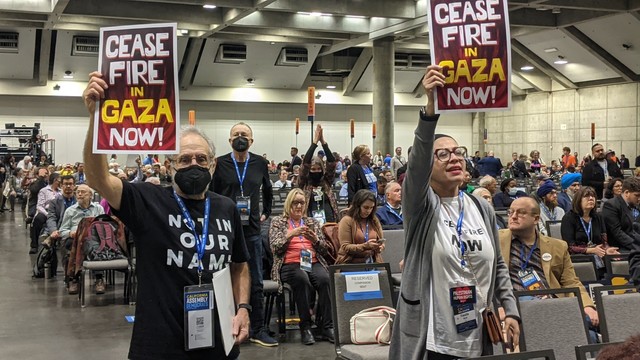 Two people with signs that say Cease Fire in Gaza Now! on the floor of the convention center