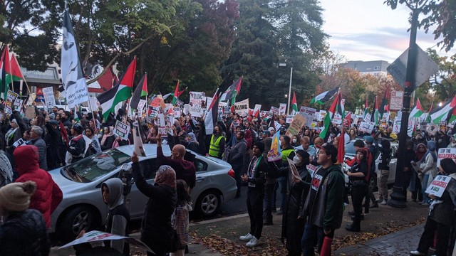 Hundreds of protesters waving signs and Palestinian flags marching down the street.