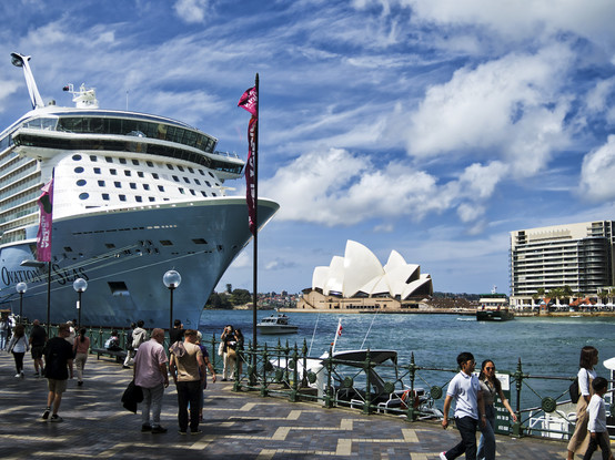 The bow of a massive cruise ship docked in Sydney Harbour, with the Opera House in the background