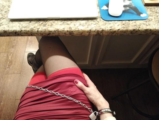 A closeup of a crossdresser's crossed legs in a red miniskirt with handcuffs on one wrist