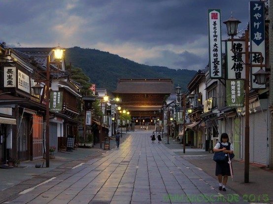 Twilight on the road leading to Zenk┼Ї-ji temple. Students can be seen in the foreground and background, perhaps on their way home. To the left and right, traditional houses line a cobbled path.

In the center at the end of the path is the temple and behind it a mountain.
