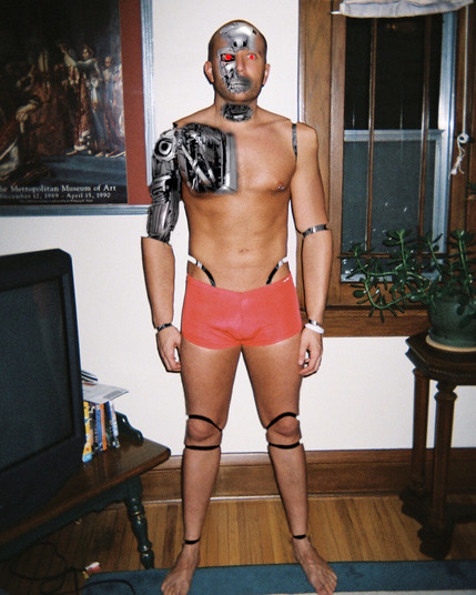 A robot with segmented limbs stands in red tights facing the camera. It's right shoulder and bicep skin and facial skin are torn off, revealing metallic endoskeleton components underneath.