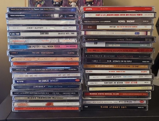2 stacks of 34 CDs total sit on a shelf. Artists include Amerie, Jewel, Tom Petty, Jimmy Buffett, Ray Charles, Case, and more