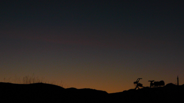 A bicycle silhouetted against a dim red and blue Montana sunset with the Beartooth mountains on the horizon