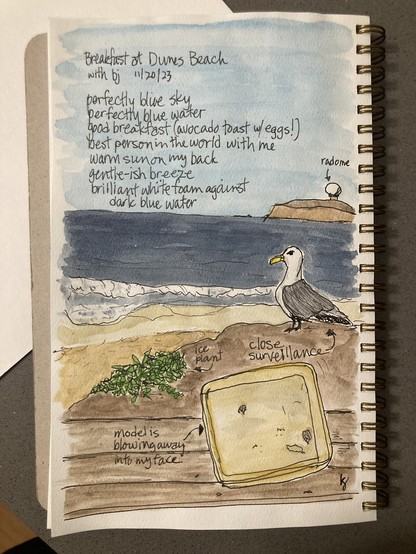 Watercolor sketch in a spiral-bound sketchbook. Perspective is from a picnic table on a bluff overlooking a beach with some foamy waves, blue water, cloudless blue sky, Pillar Point and its radome, and a seagull at the edge of the bluff. Half of a to-go box is on its edge facing us. A handwritten caption with arrow pointing to it says “model is blowing away into my face.” Handwritten by the seagull is “close surveillance.” The radome also has a caption and arrow identifying it as such. 

Handwritten at the top in the sky is:
Breakfast at Dunes Beach
With bj 11/20/2023

Perfectly blue sky
Perfectly blue water
Good breakfast (avocado toast w/ eggs!)
Best person in the world with me
Warm sun on my back
Gentle-ish breeze
Brilliant white foam against dark blue water