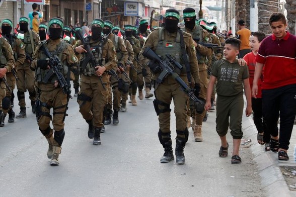 Palestinian resistance fighters marching in a street to the right children march alongside