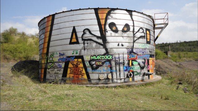 Large industrial storage tank with skull graffiti and tags. A Sunny day