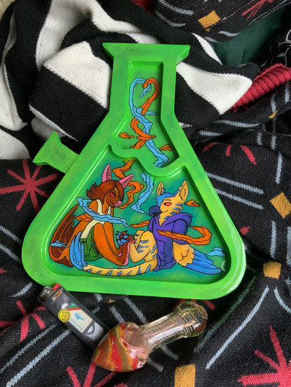 Photo of a bong-shaped rolling tray painted in bright green, with two anthro characters in the lower part of the bong, smoking together. On the right is an anthro bat, and an anthro gryphon on the right, with smoke in orange and blue wisps swirling around them. In front is a lighter and a pipe for scale.