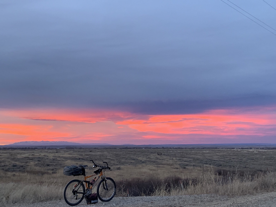 The Crazy Mountains and a vivid sunset seen over brown winter pastures with an orange bicycle in the foreground