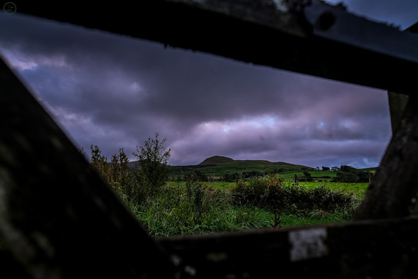 Wooden gate used as framing for view over fields towards mountains. Heavy storm cloud filled sky above