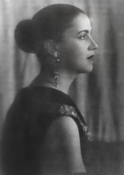 a black and white photograph of the artist, she is looking to the right , her dark hair is pulled into a bun, she wears a nice sleeveless dress and ornate earrings