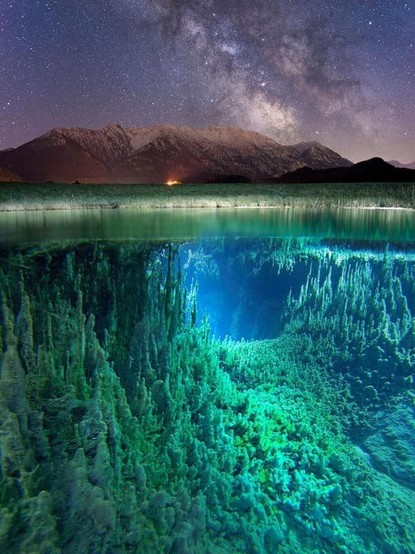 A composite image featuring the Milky Way above a mountain ridge in the top third.. Beneath that stretch the green bank of the Isar River in Germany, and then the surface of the river. The second piece of the photograph reveals the jagged and eerily lit underwater landscape of the river.