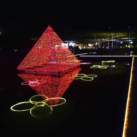 A light up red pyramid in water reflection with floral petal like lights on water