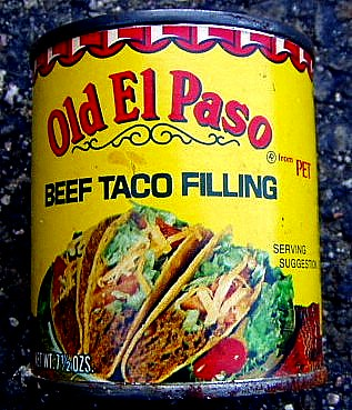 A photo of a can of Old El Paso Beef Taco Filling, probably taken in the 1980s. This was a canned taco filling for those who wanted tacos at home but were too lazy (or ignorant) to cook their own taco filling. Growing up, this was a staple item in our kitchen because Mom was a 'tacoholic'. We had tacos two, three, sometimes four times a week. (Mom was a little compulsive.) The can has a photo on the front of three tacos filled with "meat", lettuce, cheese, and tomatoes and is labeled as a "serving suggestion". Boy is that an accurate description!