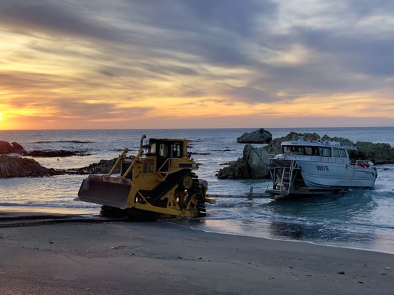Bulldozer and crayfishing boat enter the water at dawn