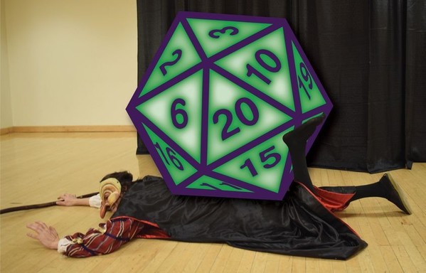 An actor poses in a dance studio of a university as the commedia dell'arte stock character of Pantalone as if knocked the ground and sat upon; a giant green and purple graphic of a D20 die is superimposed as if on top of him.
