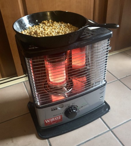 A cast iron skillet with chickpeas in it being sautéed over a kerosene room heater.