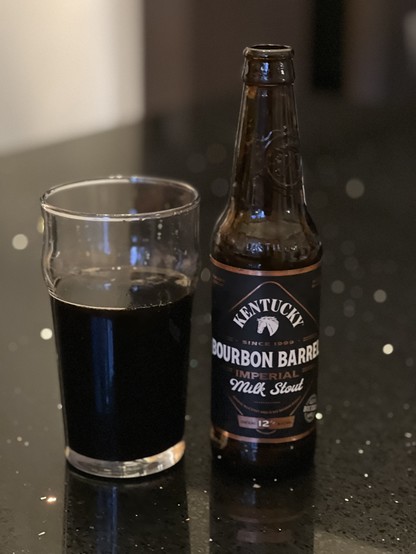 Lexington Brewingâ€™s Kentucky Bourbon barrel milk stout, dark brown/black in a pint glass with an equally dark brown bottle. The label has white lettering, a white horse head, and gold accents