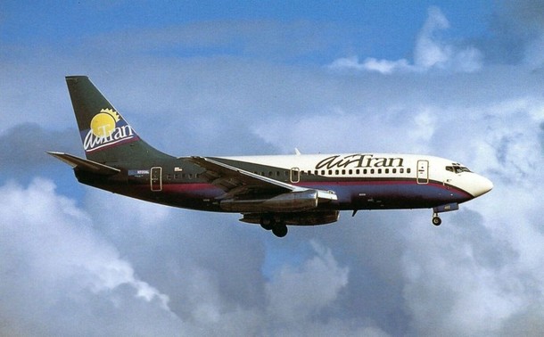An early Airtran livery on a 737 landing under white puffy clouds and a blue sky