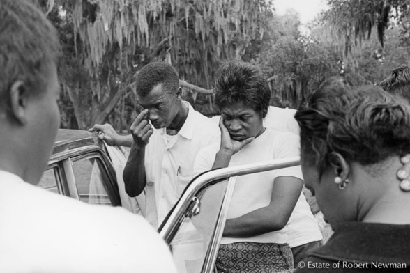 Four civil-rights workers outside a car listen to the news of president Kennedy's assassination, St. Helena Island, South Carolina. This is outside Frogmore Center, a retreat used by the Southern Christian Leadership Conference (SCLC).