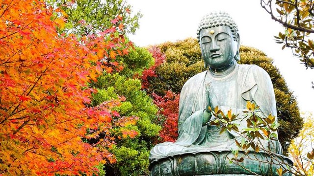 Large copper Buddha statue surrounded by fall foliage.
