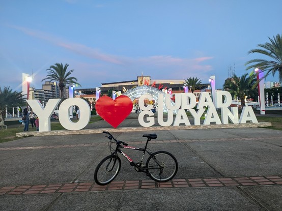 My bicycle, in the background you can see the monumental plaza of the CVG, iconic of my city, and large letters that say "I love Guayana"